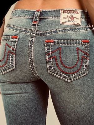 True Religion Becca Bootcut Jeans - Säljer ett par blå True Religion Becca jeans med bootcut-snitt och midwaist. Jeansen har tydliga vita och röda sömmar, samt ikoniska bakfickor med röd broderad logga. Materialet är klassisk jeans med dragkedja och knapp framtill.