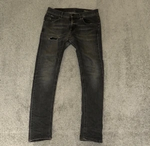 Dondup jeans  - Säljer ett par svarta dondup  jeans med  slim fit och slitningar på ena benet. Jeansen har klassisk femficksdesign, svarta detaljer och en snygg tvättad look. Perfekt för dig som gillar en smal siluett och streetstil.  Pris ej hugget i sten🪨 