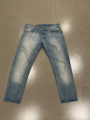 Ljusblå jeans från Dondup, storlek 33 - Säljer ett par ljusblå jeans från Dondup i storlek 33. Jeansen har en snygg tvätt med slitningar och klassisk femficksdesign. Materialet är jeans och passformen är normal med raka ben. Perfekt för dig som gillar en avslappnad stil.
