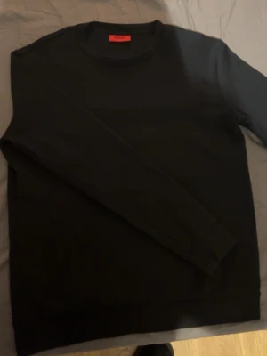 Svart sweatshirt från Hugo Boss - Svart långärmad sweatshirt från Hugo Boss med rund hals och diskret Hugo-logga i nacken. Tröjan har en clean och stilren look, perfekt för dig som gillar minimalistisk design. Mjuk bomullskvalitet och normal passform.