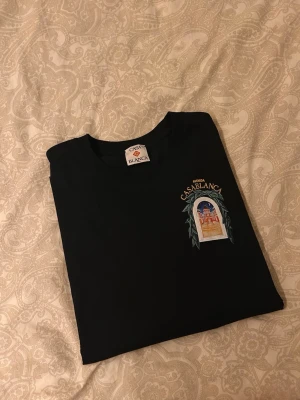 Svart t-shirt från Casablanca - Svart t-shirt från Casablanca med tryck på bröstet som föreställer en byggnad och texten 'Avenida Casablanca'. Klassisk passform och rund halsringning. Perfekt för dig som gillar stilrena plagg med unika detaljer. Storlek M men passar även L!