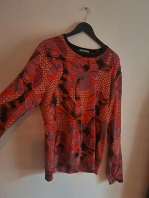 Röd mönstrad tröja från Scotch&Soda  - Unik röd tröja från Scotch&Soda färgstarkt grafiskt mönster i lila, svart och orange. Tröjan har rund halsringning och långa ärmar. Perfekt för dig som gillar statement-plagg och vill sticka ut med coola prints.