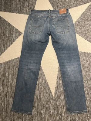Ljusblå raka jeans från Jack&Jones  - Säljer ett par ljusblå jeans från Jack&Jones med raka ben och klassisk femficksmodell. Jeansen har en snygg tvättad look och är tillverkade i bomull med lite stretch för extra komfort. Perfekta till en avslappnad stil.