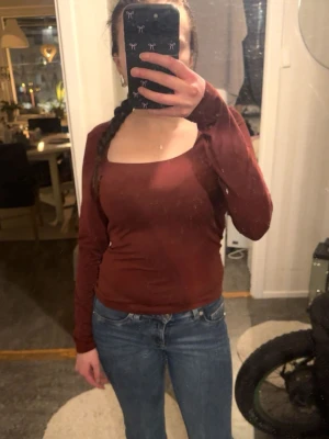 Brun långärmad topp med fyrkantig ringning - Snygg brun långärmad topp med fyrkantig ringning och figurnära passform. Perfekt att styla med jeans eller kjol för en trendig look. Materialet känns mjukt och stretchigt. Använt en gång, på julafton 2024. 