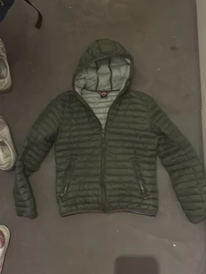 Mörkgrön dunjacka med huva - Säljer en mörkgrön dunjacka från Colmar med quiltad design och huva. Jackan är storlek 154 men passar större då jag hade den tills jag var 164. Skick 7/10 jag köpte den förra våren och används måttligt sen dess. Kontakta vid intresse!!!!