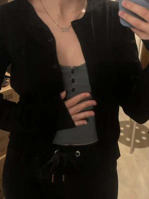 Svart basic kofta med knappar - En svart, enkel kofta med knäppning framtill. Koftan har lång ärm och rak passform, perfekt att slänga över ett linne eller t-shirt. Stilren och lätt att matcha med olika outfits.