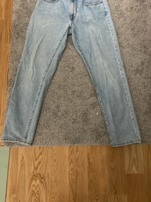 Ljusblå raka jeans i klassisk modell - Säljer ett par ljusblå jeans med rak passform och fem fickor. Jeansen har klassisk design med dragkedja och knapp framtill samt tydliga sömmar. Perfekta för en avslappnad och trendig look.