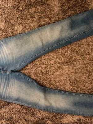 Blå slim fit jeans med skinnpatch - Snygga blå slim fit jeans med klassisk femficksdesign och en brun skinnpatch bak i midjan. Jeansen har en lätt tvättad look och smal passform som sitter tajt längs benen. Perfekta för en trendig och avslappnad stil.
