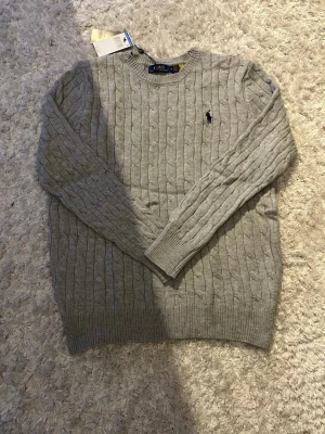 Grå stickad tröja från Polo Ralph Lauren - Säljer en snygg grå stickad tröja från Polo Ralph Lauren i storlek M. Tröjan har kabelstickat mönster. Skickas snabbt med spårbar frakt 📦. Priset är ej hugget I sten 🤩