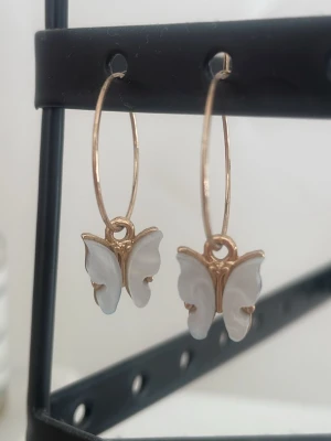 Guldiga örhängen med fjärilar - Snygga örhängen med tunna guldfärgade ringar och hängande fjärilar i vit pärlemor-look. 