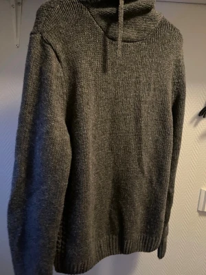 Grå stickad hoodie från Pier One - Mysig grå stickad hoodie från Pier One med huva och dragsko. Tröjan har lång ärm och ribbstickade muddar vid ärmslut och nederkant. Perfekt för kalla dagar och enkel att matcha med jeans eller mjukisbyxor.