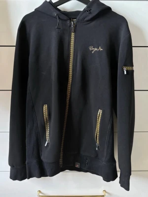 Svart loungewear-set  - Säljer ett svart loungewear-set från bourgeios avenue med hoodie och shorts. Hoodien har dragkedja, huva med snörning och fickor med gulddetaljer. Shortsen har resår i midjan, snörning och fickor. Perfekt för chill dagar hemma.