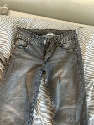 Grå jeans från Kappahl - Snygga grå jeans från Kappahl med klassisk femficksmodell och dubbla knappar i midjan. Jeansen har utsvängda ben och är tillverkade i ett mjukt denimtyg som ger en avslappnad look. Perfekta för dig som gillar stilrena och enkla jeans. PRIS KAN DISKUTERAS 