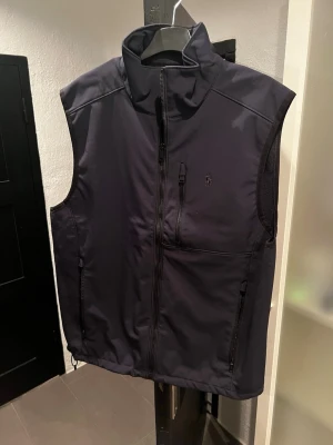 Svart väst från Ralph Lauren - Snygg svart väst från Ralph Lauren med hög krage och dragkedja framtill. Västen har tre fickor med dragkedja och diskret logga på bröstet. Perfekt för lager på lager och enkel att matcha med olika outfits.