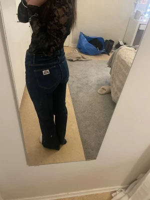 Mörkblå bootcut jeans från Wrangler - Säljer ett par mörkblå bootcut jeans från Wrangler med klassisk femficksdesign och logga på bakfickan. Jeansen har hög midja och är tillverkade i ett kraftigt denimtyg som ger en snygg passform. Perfekta för en trendig och avslappnad look.