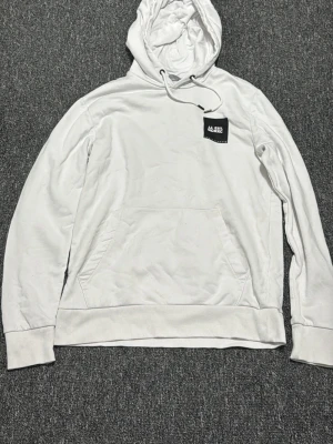 Vit hoodie med huva och magficka - Säljer en stilren vit hoodie från Lee med klassisk huva och dragsnöre. Hoodien har en stor magficka framtill och ribbade muddar vid ärmslut och nederkant. Perfekt för en avslappnad och clean look.