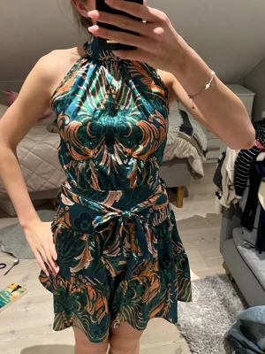 Grön och orange halterneckklänning - Säljer en superfin klänning köp i Singapore av min pappa. Perfekt passform och skönt material. Använt varsamt 2 gånger och legat skyddat sen dess.