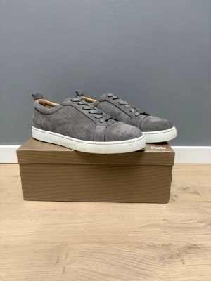Christian Louboutin suede - Snygga sneakers i grå mocka från Christian Louboutin med vita sulor och matchande grå skosnören. Skorna har en stilren och minimalistisk design med låg profil och diskreta sömmar.