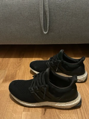 Svarta Adidas Ultraboost sneakers - Svarta Adidas Ultraboost sneakers med stickad ovandel och klassisk Boost-sula i vitt. Skorna är i storlek 40 2/3 och är 100% äkta men är slitna och är trasiga på framsidan. Hör av er ifall ni har frågor eller är intresserade!🙌 Priset går att diskutera. Ordinarie pris 2000kr