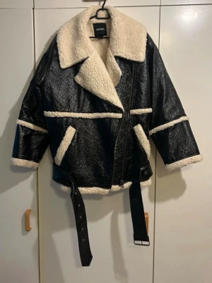 Svart teddyjacka från Monki - Snygg svart teddyjacka från Monki med stora kragar och detaljer i beige fuskpäls. Den har en oversized passform.