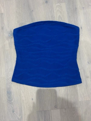 Blå bandeau tubtopp från SHEIN - Snygg blå bandeau tubtopp från SHEIN i stretchigt material med vågigt strukturmönster. Toppen är ärmlös och sitter tight mot kroppen, perfekt för att skapa en trendig look.