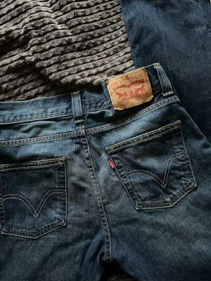 Levi's 506 blå jeans W31 L34 - Klassiska blå jeans från Levi's modell 506 med raka ben och femficksdesign. Snygga kontrastsömmar och ikonisk läderpatch bak i midjan. Jeansen har normalhög midja och är tillverkade i slitstark denim. Perfekta för en avslappnad och tidlös look.