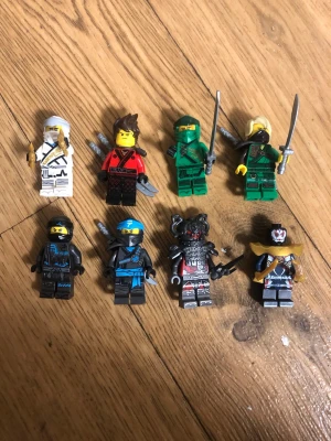 Lego Ninjago figurer med tillbehör - Säljer ett set med åtta Lego Ninjago minifigurer i olika färger och stilar, inklusive svärd och andra tillbehör. Figurerna är detaljerade med dräkter i vitt, rött, grönt, svart och blått samt en samuraj i svart och rött. Perfekt för samlare eller lek.