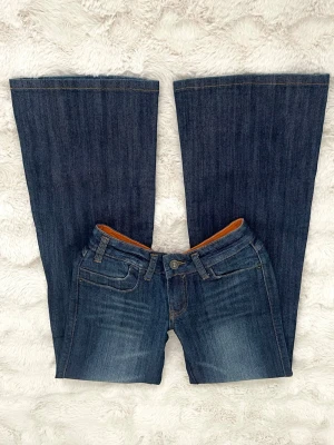 Blå bootcut jeans med broderade fickor - Snygga blå jeans med bootcut-modell och broderade detaljer på bakfickorna. Jeansen har klassisk femficksdesign, orange insida i midjan och är tillverkade i jeansmaterial. Perfekta för dig som gillar en retroinspirerad look.