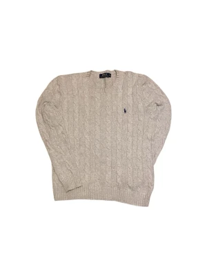 Beige kabelstickad tröja Polo Ralph Lauren - Kabelstickad beige tröja från Polo Ralph Lauren med klassisk marinblå logga broderad på bröstet. Tröjan har rund halsringning, långa ärmar och ribbade muddar. Perfekt för dig som gillar tidlös och stilren design.