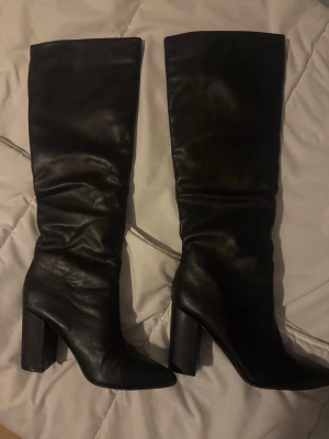 boots med klack - Säljer ett par svarta höga stövlar i slätt skinnimitation med bred klack och spetsig tå. Stövlarna har en trendig, lite rynkad look och passar perfekt till både jeans och kjol. Snygg och stilren design som lyfter varje outfit. använda 1 tillfälle 