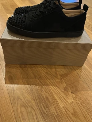 Svarta spikes-sneakers från Louboutin - Säljer ett par svarta sneakers från Christian Louboutin med mattsvarta nitar över tån. Skorna har en låg siluett, svarta skosnören och ovandel i mocka. Snygg och edgy design som sticker ut med sina detaljer. Jätte bra skick 