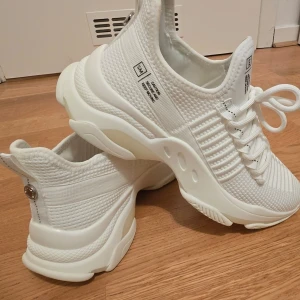 Vita chunky sneakers Steve Madden - Säljer ett par helvita Steve Madden sneakers med chunky sula och stickad mesh-ovandel. Skorna har vita snören, ribbade detaljer och texttryck på sidan. Snygg modern design som passar till streetwear och casual outfits. Lätta och bekväma med sportig känsla.