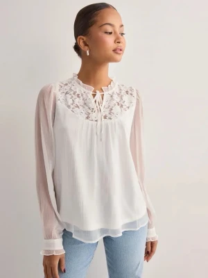 Vit blus med spets och knytning - Snygg vit blus med transparenta långärmar och vacker spetsdetalj upptill. Blusen har en liten volangkrage och knytning vid halsen. Tillverkad i ett lätt och luftigt material som ger en romantisk känsla. Slutsåld överallt!! Nypris är 500kr!! Helt oanvänd!!