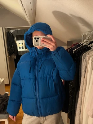 Blå pufferjacka med huva - Hejsan! Säljer en blå pufferjacka från HM med dragkedja och stor huva. Jackan har två sidofickor. Perfekt för kalla dagar och har en avslappnad passform. Materialet är syntetiskt och jackan är riktigt fluffig och varm! Skriv för fler bilder samt frågor!☺️