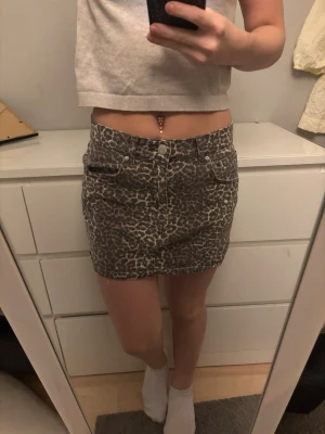 Leopardmönstrad kortkjol i denim - Säljer en snygg kortkjol med leopardmönster i beige och bruna toner. Kjolen har klassisk jeansmodell med fickor fram och bak samt knapp- och dragkedjestängning. Perfekt för dig som vill sticka ut lite extra.