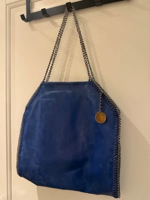 Blå väska  - Imitation av Stella Mc. Cartney väskan i klarblå färg! Super fin men använder sällan. Har inga skador och det är bara å skriva för fler bilder. Den är medelstor, går att få ner dator och lite till.