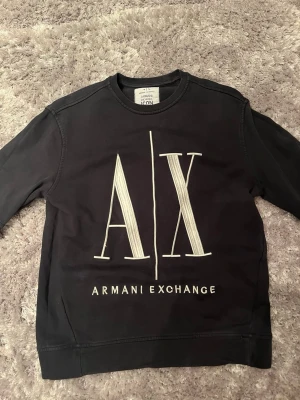 Svart sweatshirt från Armani Exchange - Cool svart sweatshirt från Armani Exchange med stort vitt A|X-tryck och logga framtill. Klassisk rund halsringning och långa ärmar. Perfekt för en avslappnad och trendig look. Skick 9/10. Vid eventuella frågor är det para skicka ett dm! 🤝