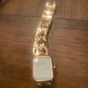 Guldfärgad Eichmüller klocka - Snygg guldfärgad klocka från Eichmüller med fyrkantigt klocka ur i ny skick och högsta kvalitet.