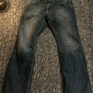 Archive jeans - Snygga blå jeans från D.N.M Jeans med klassisk femficksdesign och flared ben. Jeansen har en mörk tvätt med lätt slitning och kontrastsömmar. Passar dig som gillar en enkel och tidlös look med straight fit.