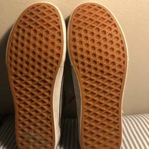 Grå Vans Old Skool sneakers - Säljer ett par grå Vans Old Skool sneakers med vit sula och klassisk vit sidostripes. Skorna har snörning och är tillverkade i mocka och canvas. Yttersulan är i gummi med det typiska rutmönstret. Perfekt för dig som gillar streetstyle och skate.