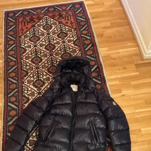 Marinblå Maya dunjacka från Moncler - Säljer en marinblå dunjacka från Moncler med glansig finish och huva. Jackan har dragkedja framtill och två sidofickor med dragkedja. Insidan har Monclers klassiska serietidningsmärke. Perfekt för kalla dagar. Vid frågor vänlig kontakta mig! 👍🏼