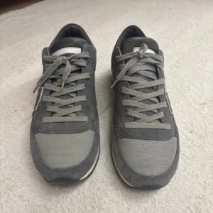 Grå Philippe Model sneakers strl 40 - Snygga grå sneakers från Philippe Model, tillverkade i Italien. Skorna har en mix av mocka och textil, med klassisk snörning och rund tå. Sidan pryds av den ikoniska skölden och sulan är platt med svart mönster undertill. Perfekt för dig som gillar stilrena och exklusiva sneakers. Perfekt nu inför vintern till dig som inte vill bli blöt om fötterna när snön kommer.