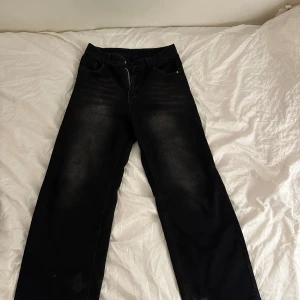 Svarta wide jeans  - Svarta jeans med breda ben och coola slitningar vid bensluten. Jeansen har klassisk femficksdesign och en mörk tvätt med lätt faded effekt framtill och baktill. Perfekt för dig som gillar en avslappnad och trendig look.