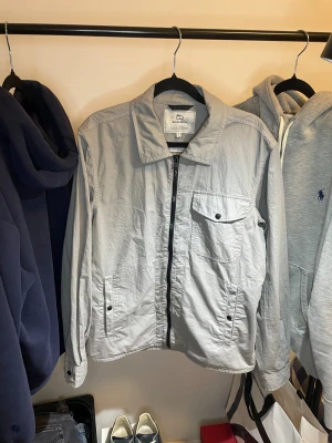 Ljusgrå vindjacka från Woolrich S - Snygg ljusgrå vindjacka från Woolrich i storlek S. Jackan har klassisk krage, dragkedja framtill, bröstficka med knapp och två sidofickor. Tillverkad i bomull och polyester, perfekt för vår och höst. Enkel och stilren design som passar till det mesta.