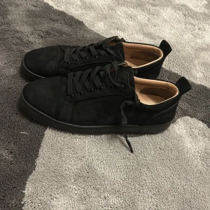 Christian Louboutin svarta sneakers mocka - Svarta sneakers från Christian Louboutin i mjuk mocka med klassisk röd sula och svarta snören. Snygg och stilren design med rund tå och platt sula, perfekt för dig som gillar exklusiva detaljer och streetstyle. Ingen box morsan slängde den tyvärr folket!