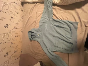 Blå hoodie Broken Planet XS - Säljer en ljusblå hoodie från Broken Planet i storlek XS. Hoodien har broderad text på bröstet och ärmen, samt stora magfickor och ribbade muddar. Materialet är mjuk bomull och polyester, perfekt för chill dagar. Snygg och enkel stil med huva.