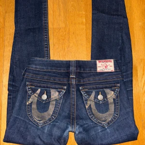 True Religion Becky jeans, mörkblå, stl 24 - Va inte blyga med att pruta eller fråga om mer information. :).                                                       Säljer ett par mörkblå True Religion Becky jeans med ikoniska broderade fickor och kontrastsömmar. Modellen har låg midja och skinny passform, tillverkade i klassiskt jeansmaterial. Märkespatch bak och coola detaljer på fickorna.