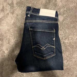 Replay Anbass jeans   - Snygga Replay Anbass jeans i mörkblå tvätt med kontrastsömmar och klassisk femficksdesign. Slim fit-modell med raka ben och detaljerad brodering på bakfickan. 