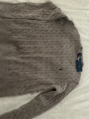 Beige kabelstickad tröja Ralph Lauren - Snygg beige kabelstickad tröja från Ralph Lauren med klassisk rund hals och broderad marinblå logga på bröstet. Unisex!!.