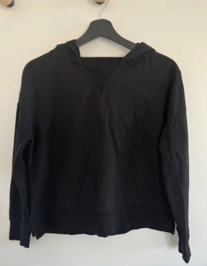 Svart hoodie med slits i sidan - Hoodien har ribbade muddar och en snygg slits i sidan vid nederkanten. Enkel och clean design som funkar till många stilar. Perfekt för dig som gillar basic och bekvämt.